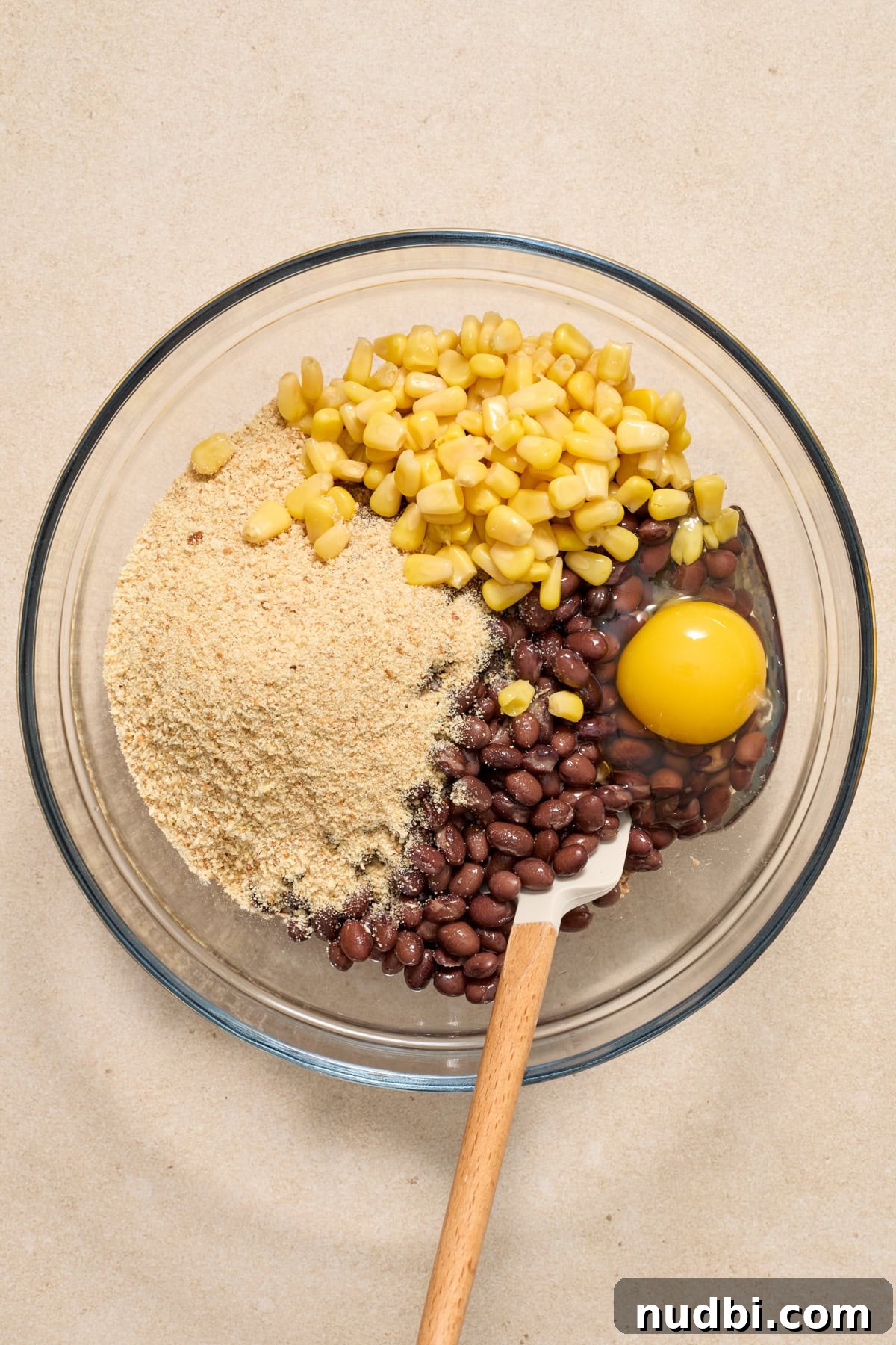 Spicy Cilantro Lime Black Bean Burgers 6 Breadcrumbs, black beans, eggs and corn added to mixing bowl with spatula.