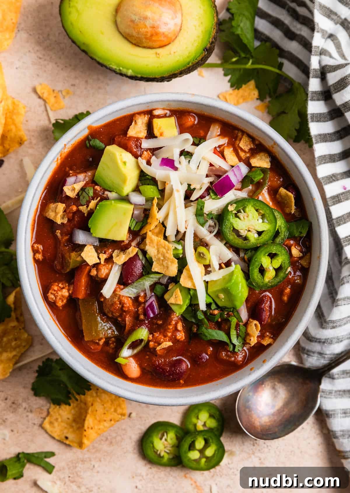 Hearty Turkey Chili Recipe for Cozy Weeknight Dinners 2 Overhead view of bowl of simple turkey chili topped with cilantro, avocado, corn chips and cheese.