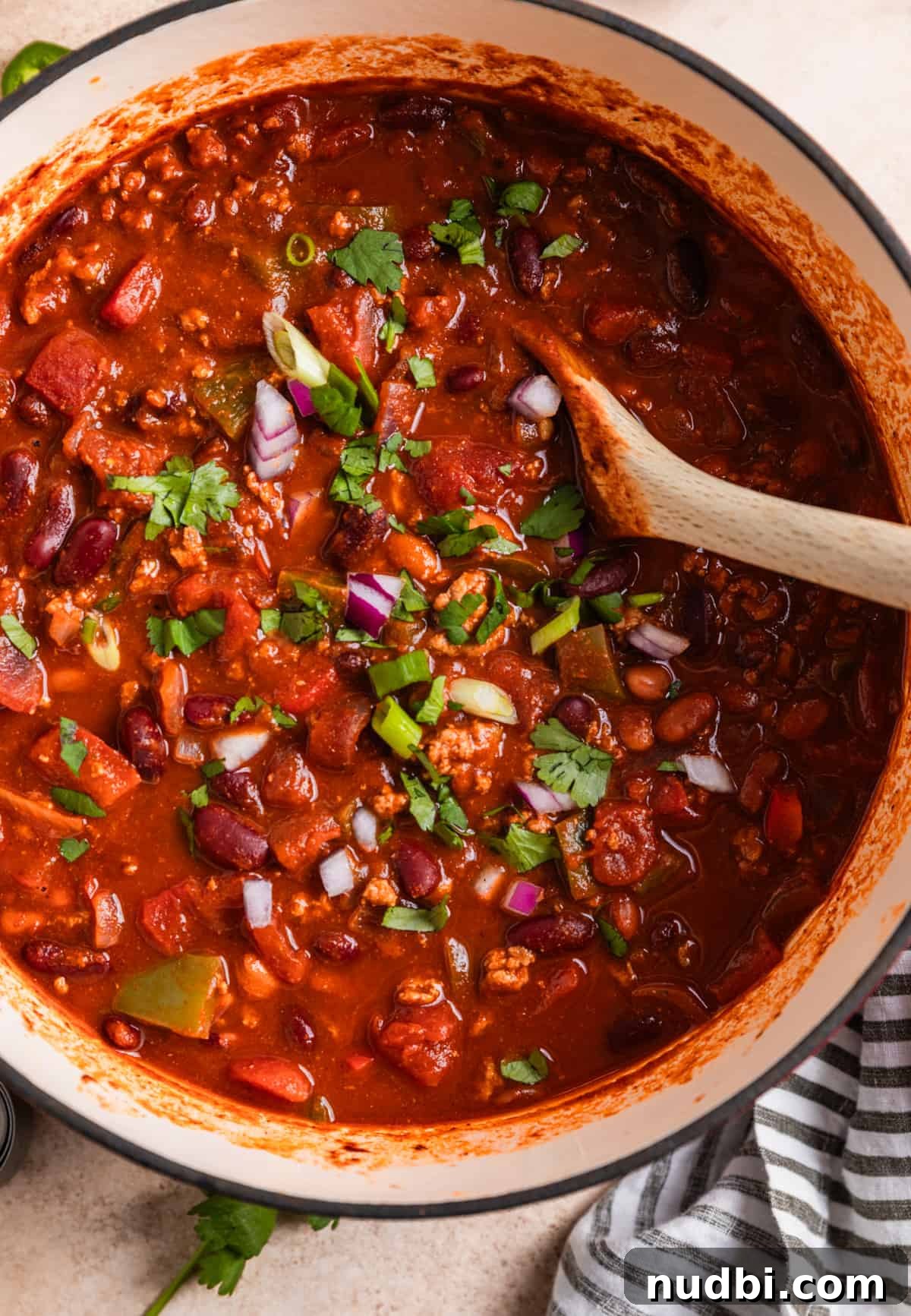 Hearty Turkey Chili Recipe for Cozy Weeknight Dinners 3 Large pot with turkey chili and wooden spoon topped with freshly chopped onion and cilantro.