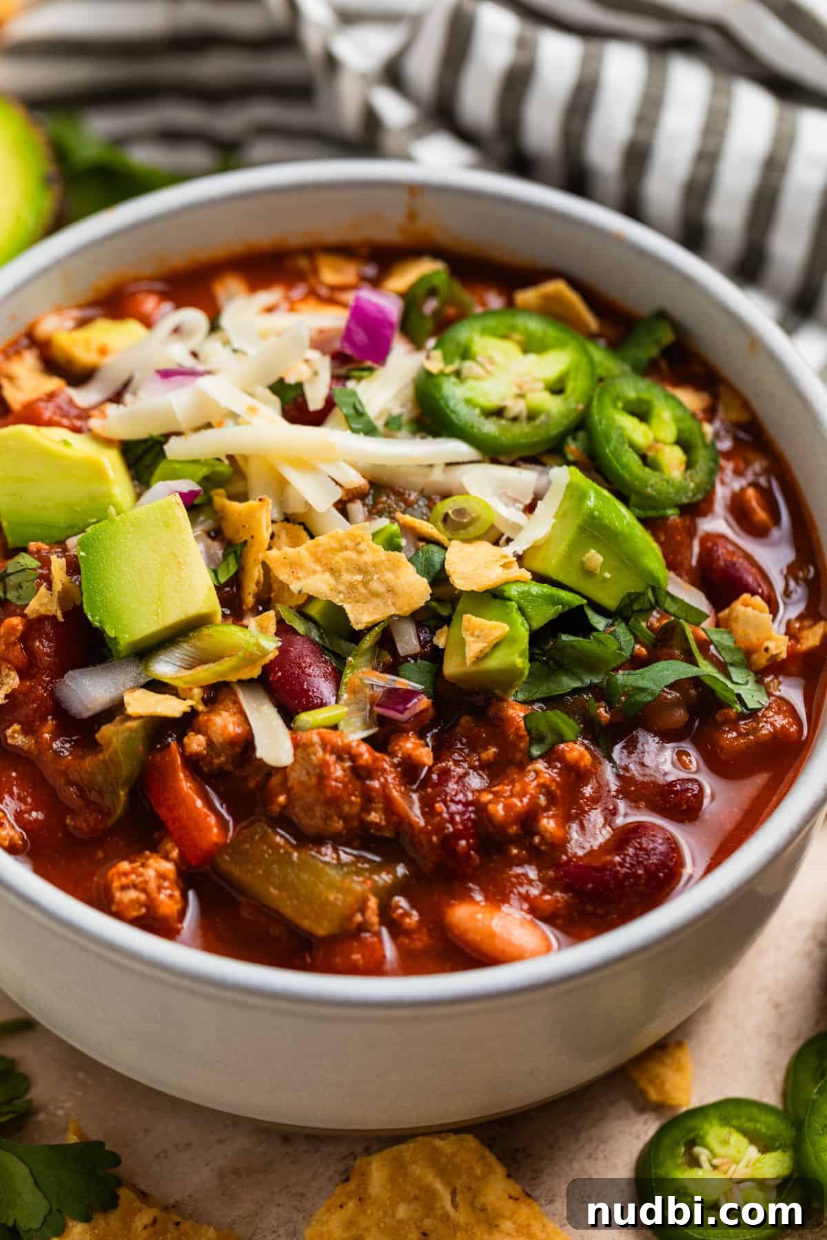 Hearty Turkey Chili Recipe for Cozy Weeknight Dinners 4 Bowl with chili topped with jalapeño, onion, avocado, cheese, etc.