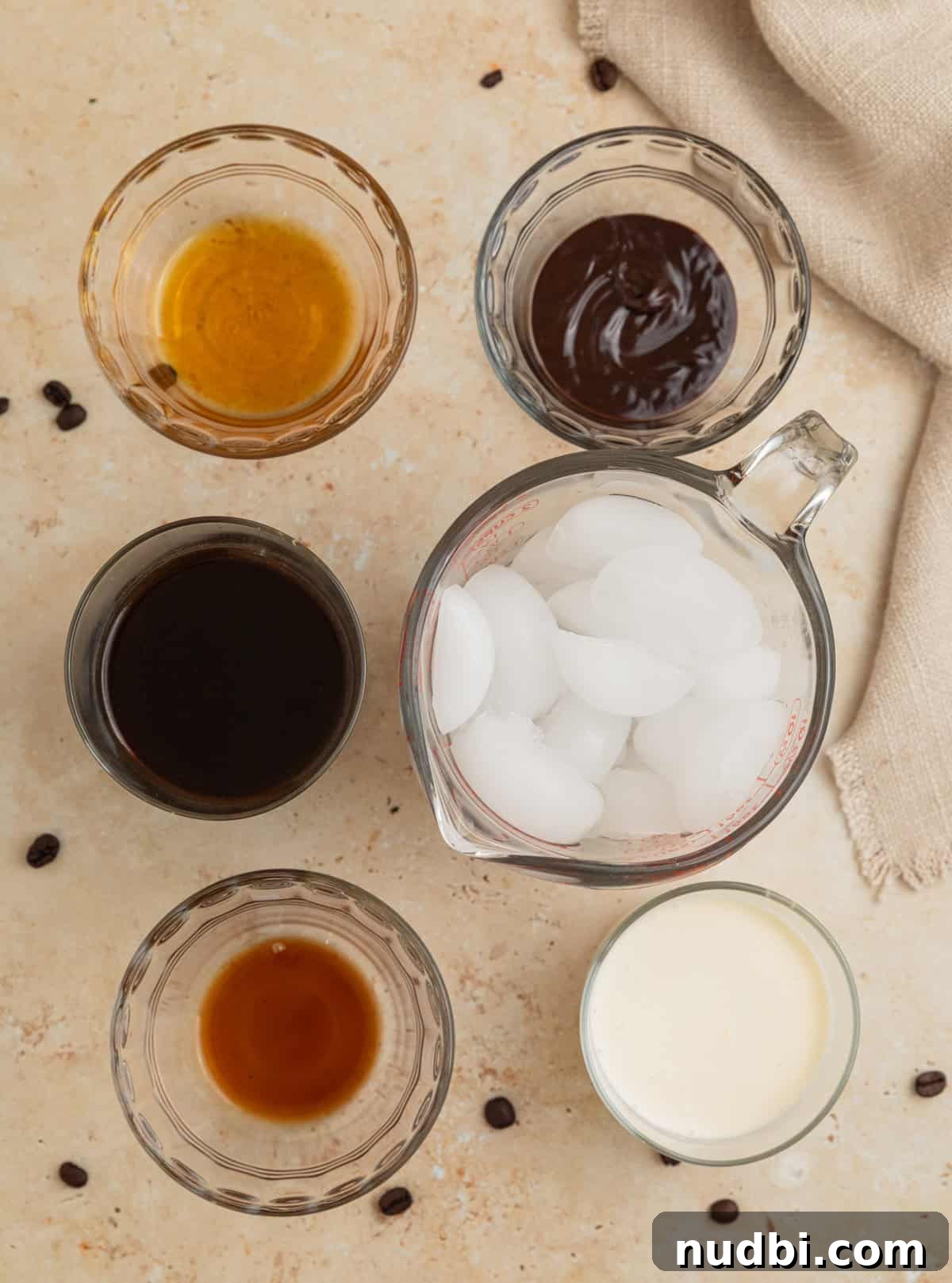Homemade Mocha Frappuccino Recipe for Café-Style Iced Coffee 3 Ice, vanilla, coffee and other ingredients on surface.