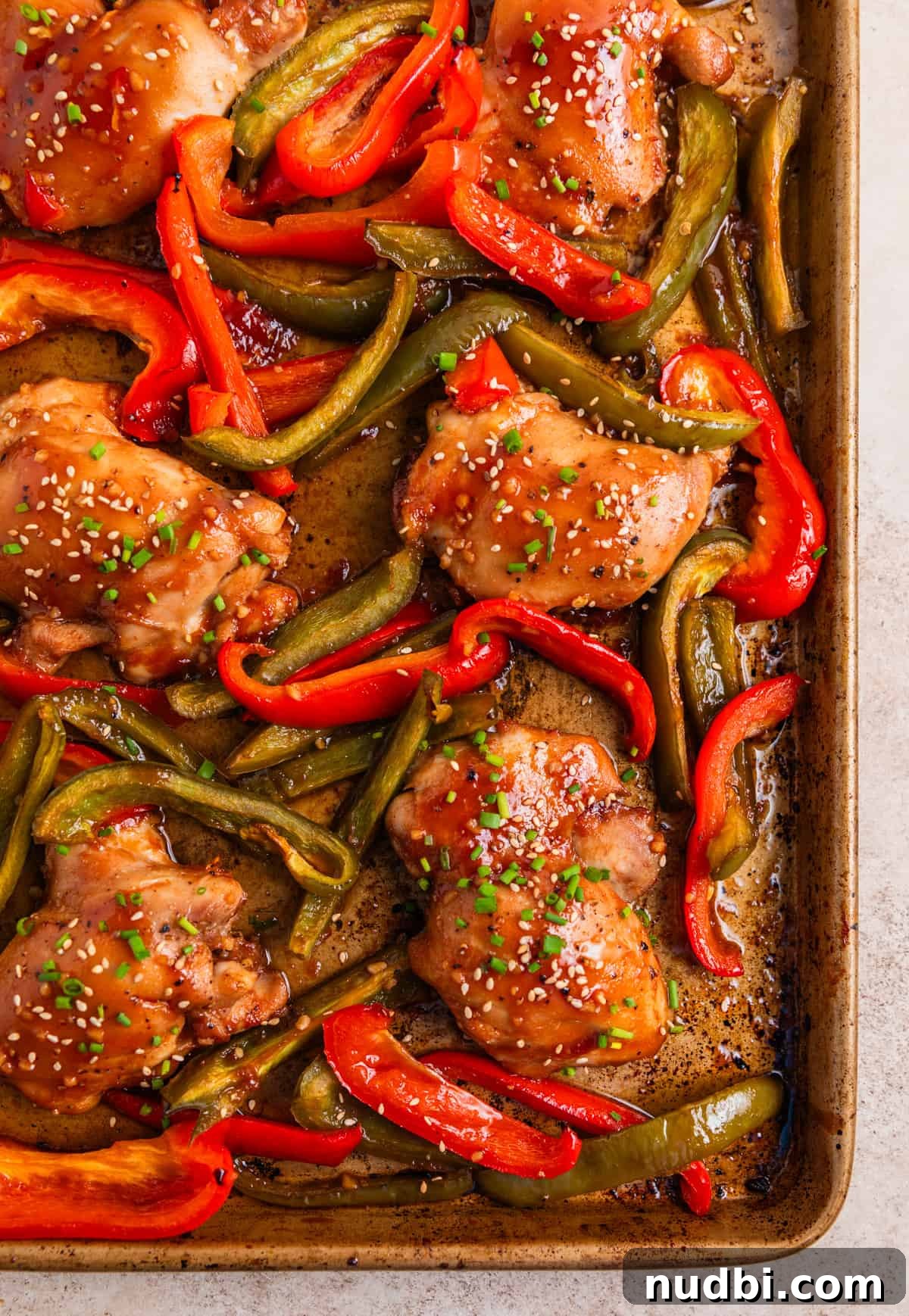 Honey Garlic Sheet-Pan Chicken Thighs Recipe 2 Chicken thighs and red and green bell peppers baked on sheet pan and topped with chives and sesame seeds.