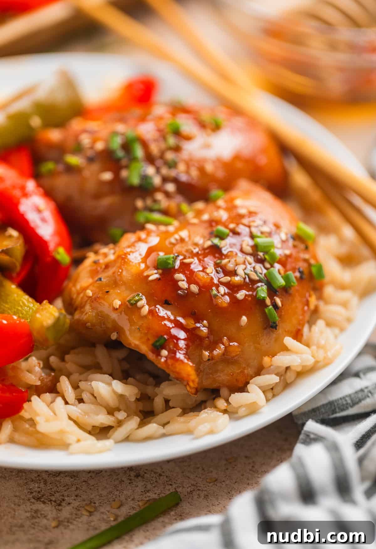 Honey Garlic Sheet-Pan Chicken Thighs Recipe 3 Honey garlic chicken thighs with peppers over rice on white plate.