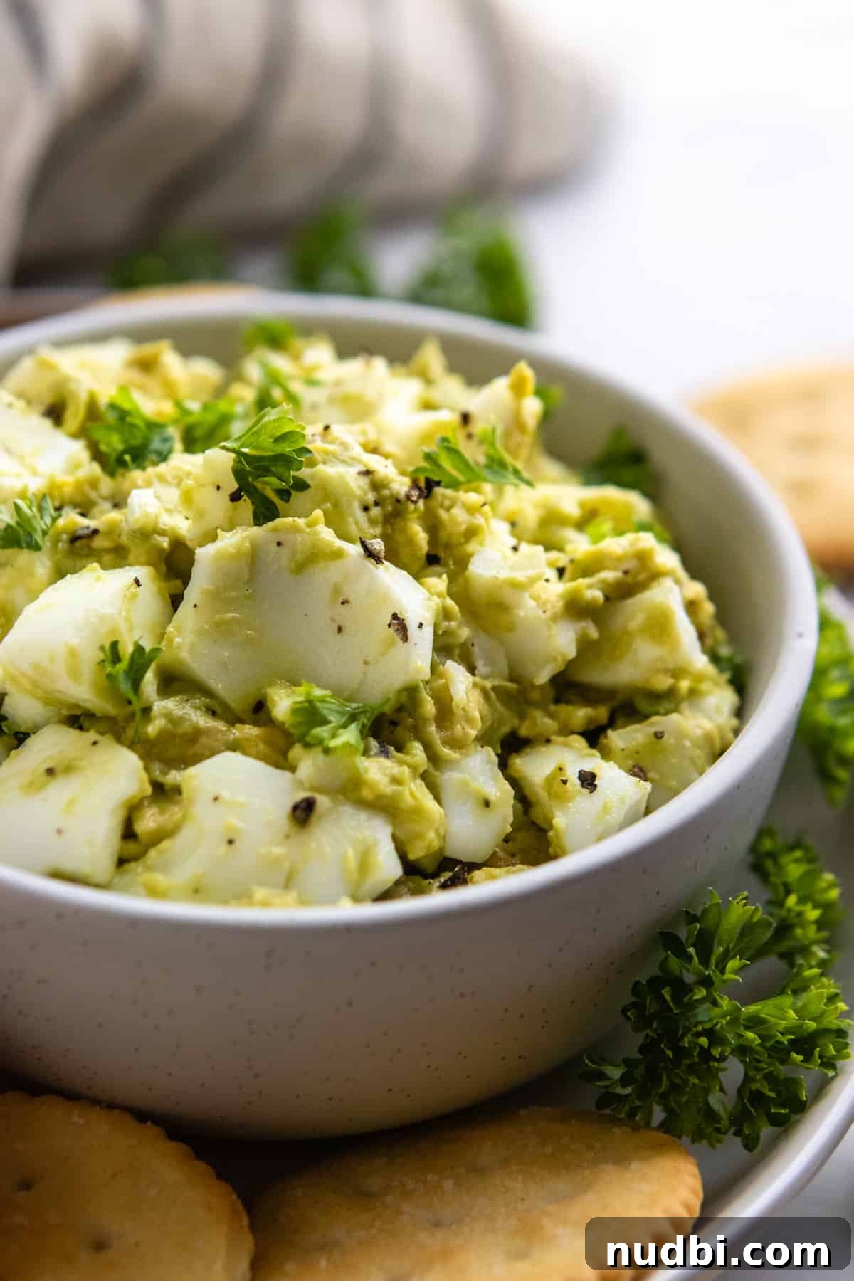 Avocado Egg Salad in bowl with crackers and fresh parsley.