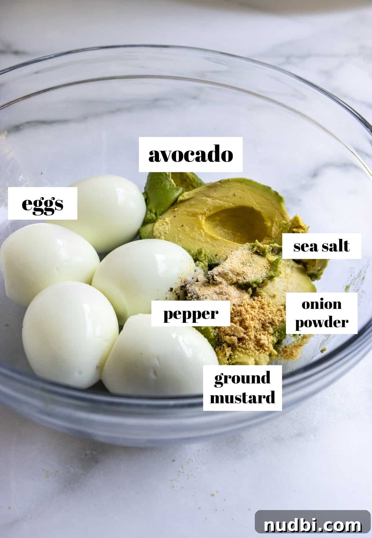 Eggs, avocado, seasonings in glass mixing bowl.