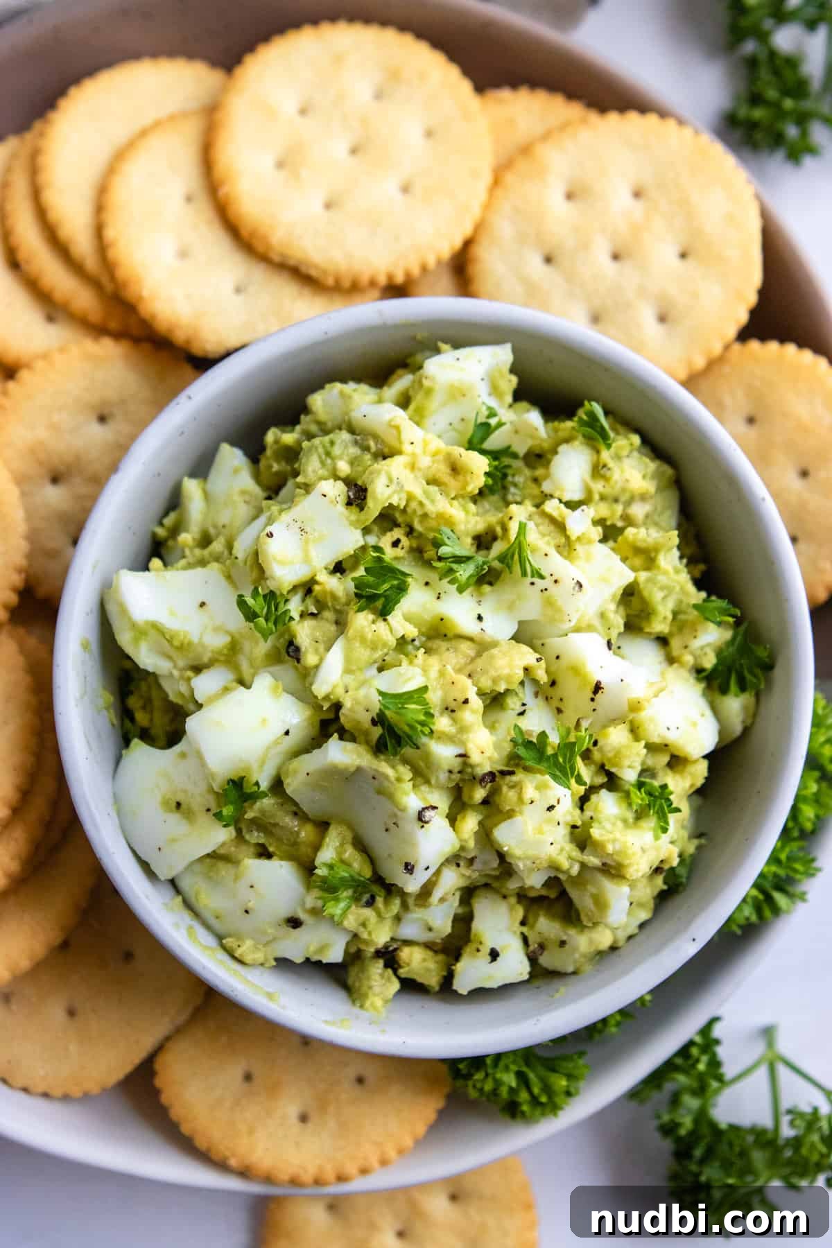 Overhead view of avocado egg salad in bowl with crackers.