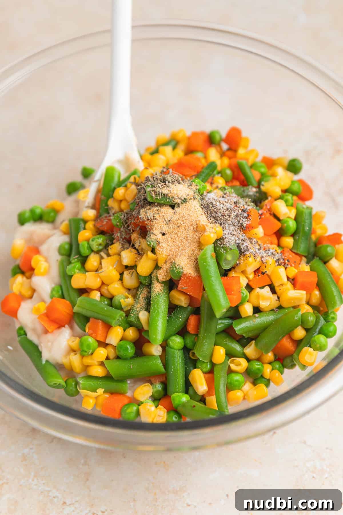 Savory Ground Beef Pot Pie Recipe with Flaky Crust 4 Mixed vegetables, cream of potato soup, seasoning and spoon in glass mixing bowl.