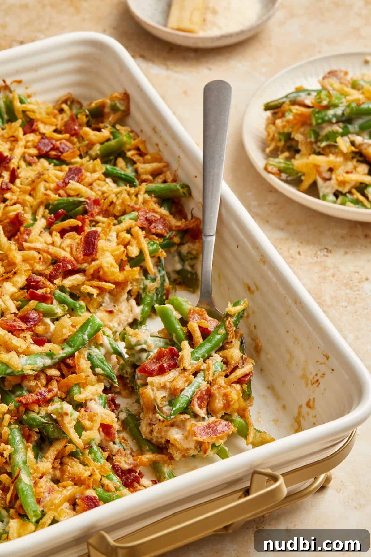 Cheesy Bacon Green Bean Casserole Recipe with Crispy Topping 2 Green bean casserole with chopped bacon in baking pan with serving spoon scooping up a serving.