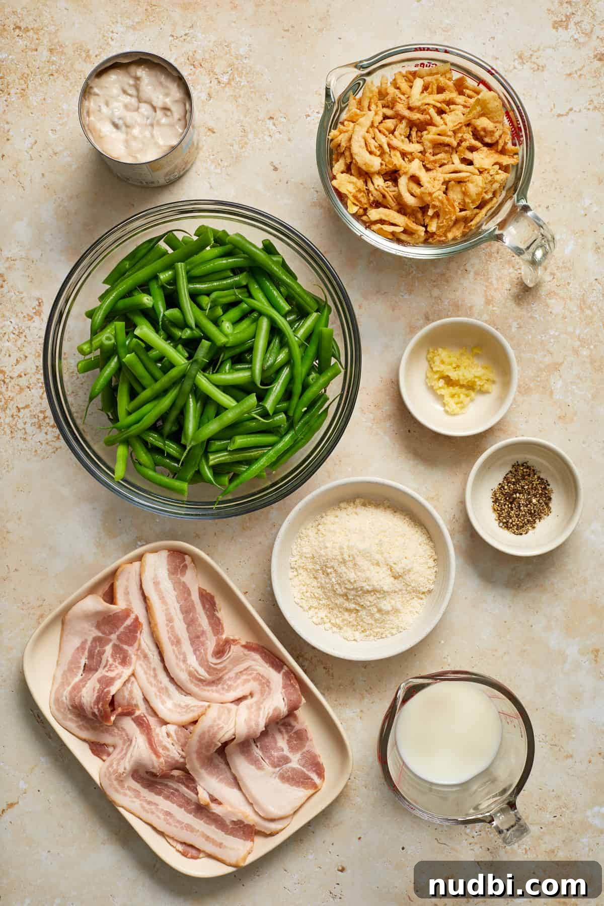 Cheesy Bacon Green Bean Casserole Recipe with Crispy Topping 3 Fried onions, soup, green beans, bacon and other ingredients for recipe arranged on surface.