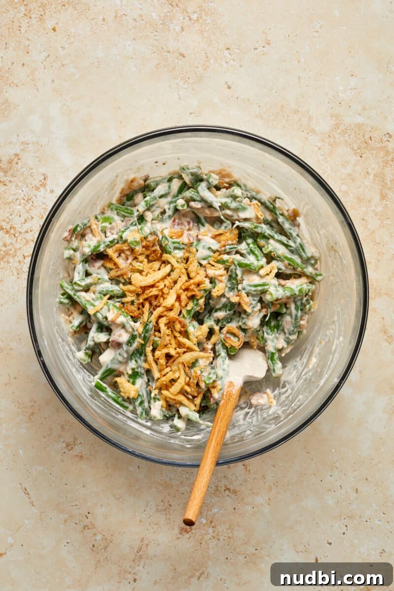 Cheesy Bacon Green Bean Casserole Recipe with Crispy Topping 6 Green beans and fried onions stirred into mixing bowl.