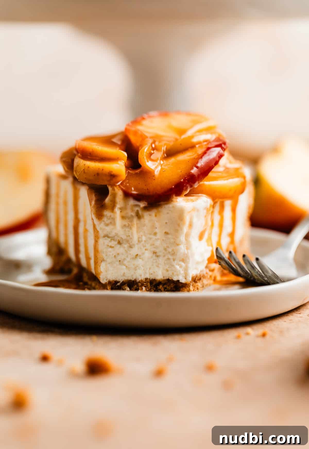 No-Bake Caramel Apple Cheesecake Recipe for Fall Gatherings 2 Slice of caramel apple cheesecake on white plate with fork marks and caramel dripping down each side.