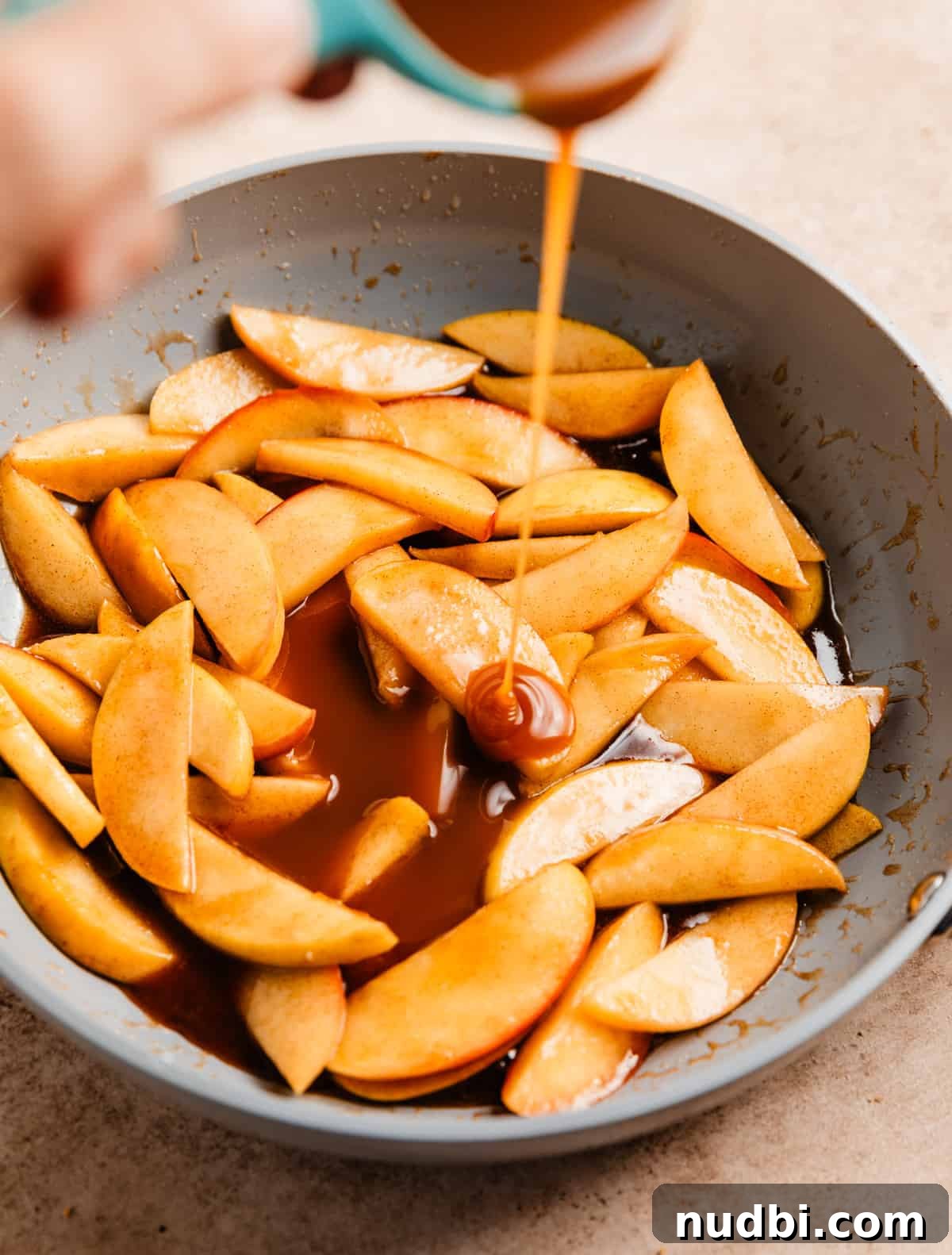 No-Bake Caramel Apple Cheesecake Recipe for Fall Gatherings 16 Caramel sauce pouring from measuring cup into fried cinnamon apples.