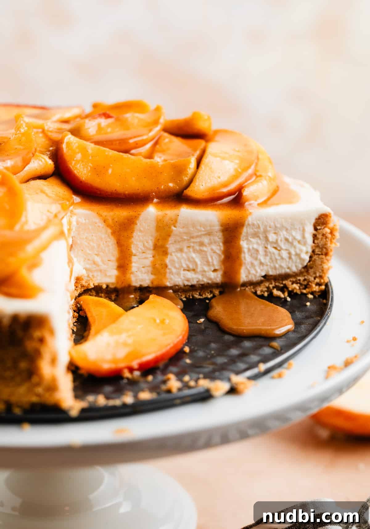 No-Bake Caramel Apple Cheesecake Recipe for Fall Gatherings 19 Cheesecake with slice cut out topped with sliced caramel apples and caramel dripping down the sides.