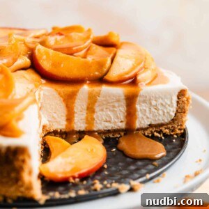No-Bake Caramel Apple Cheesecake Recipe for Fall Gatherings 20 Cheesecake on cake stand with slice cut out to expose the texture of the cheesecake with caramel apples on top.