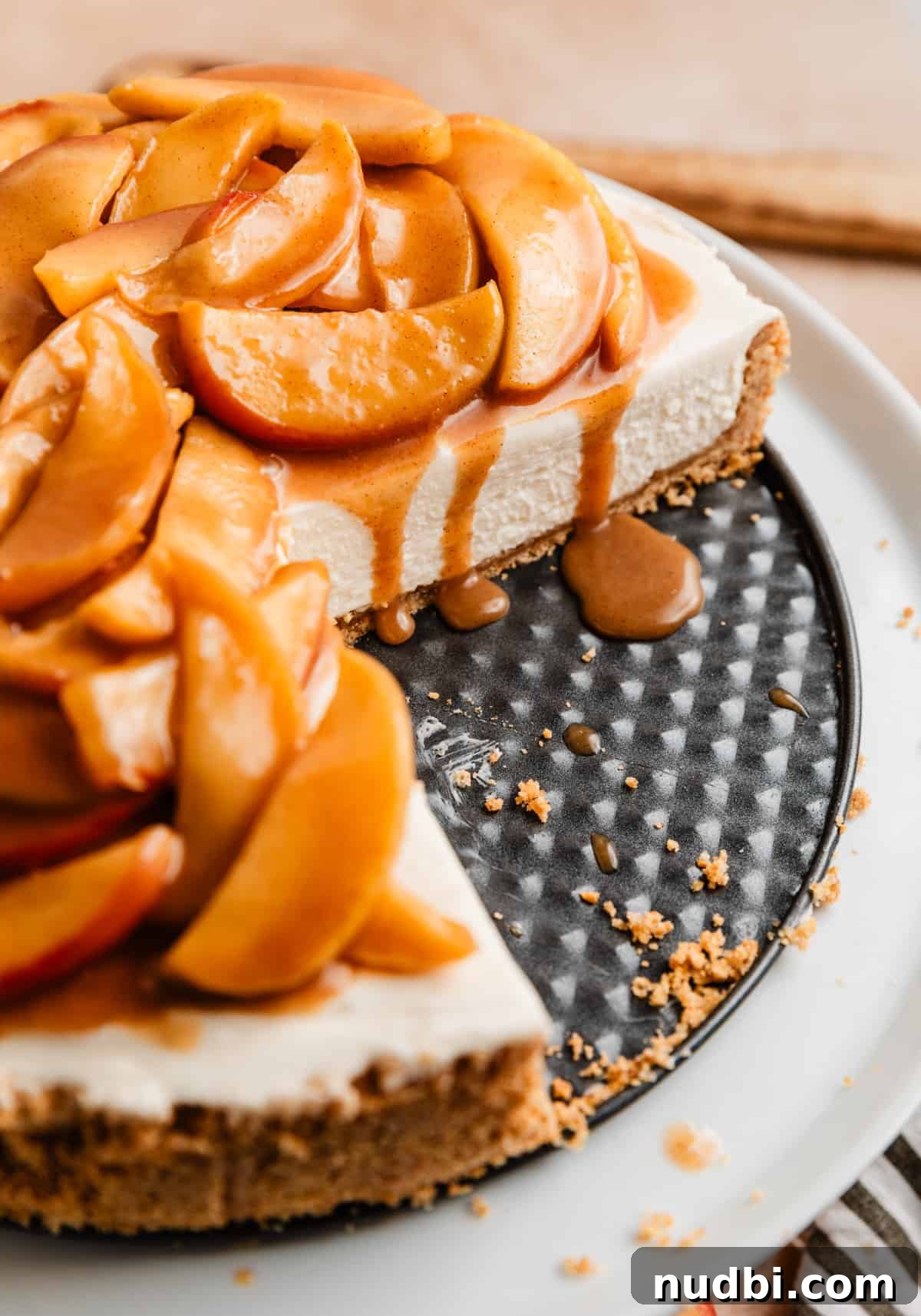 No-Bake Caramel Apple Cheesecake Recipe for Fall Gatherings 3 Caramel apple no bake cheesecake with slices taken out and caramel drizzling over the sides on cake stand.