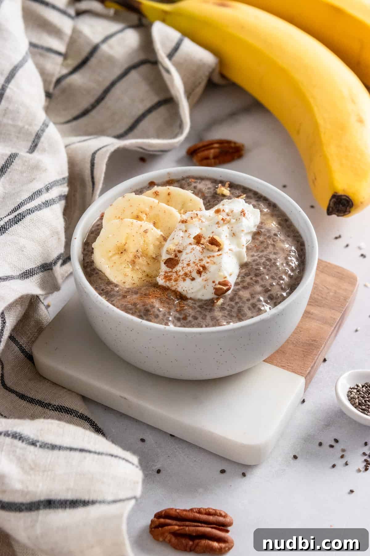 Creamy Banana Chia Seed Pudding Recipe for Breakfast & Snacks 6 Chia pudding in bowl on coaster with bananas and pecans in the background.