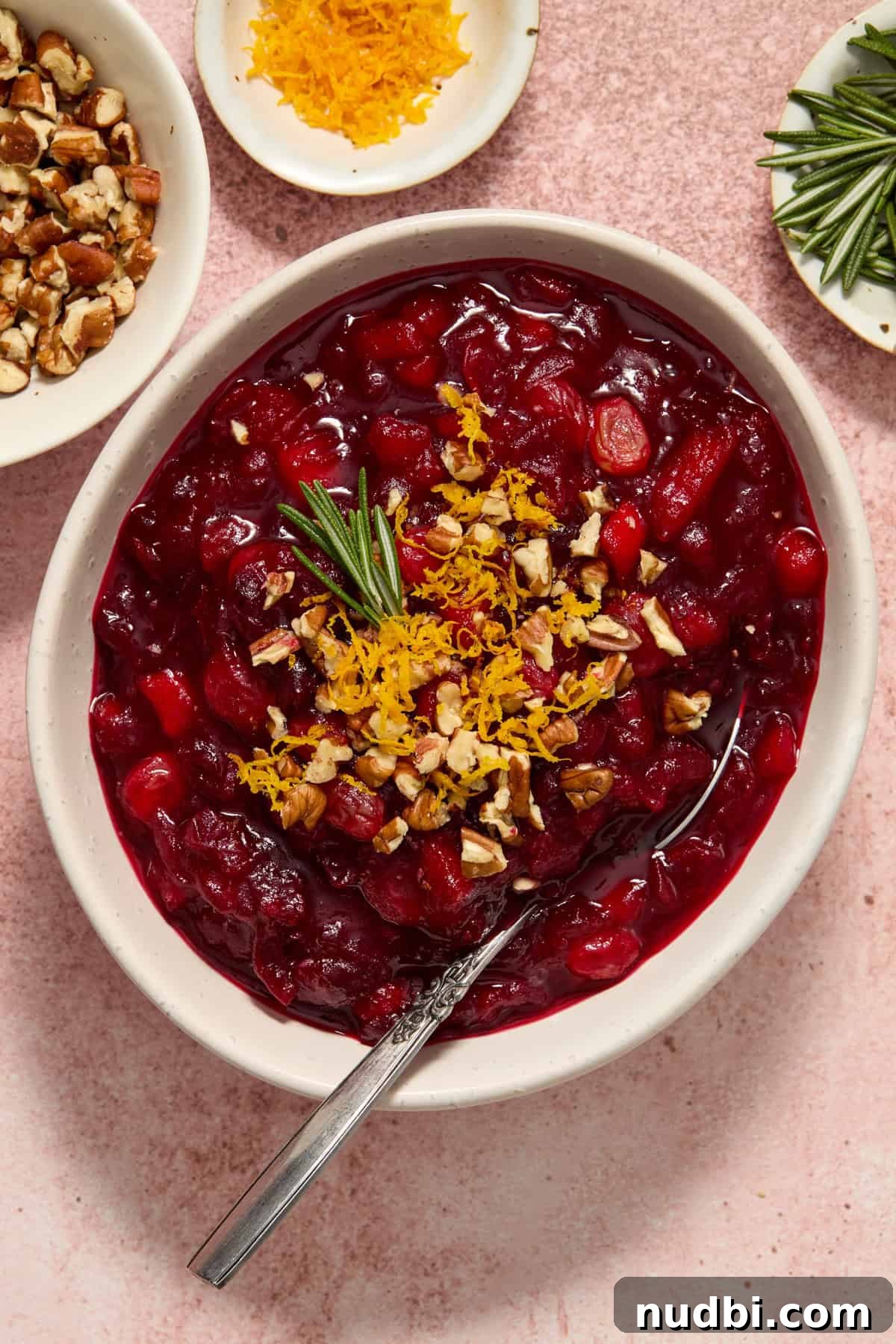 Cranberry Apple Chutney Recipe for Holidays and Leftovers 2 Bowl of apple cranberry chutney with spoon, topped with orange zest, pecans and herbs.