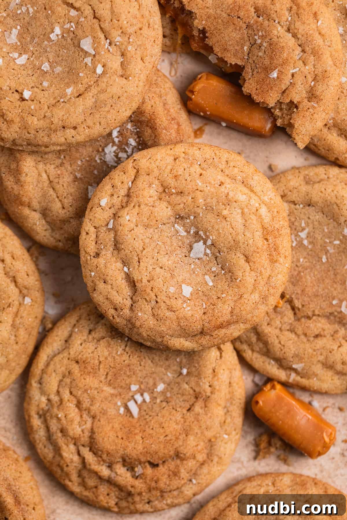 Chewy Snickerdoodle Cookies Filled with Caramel 3 Caramel filled snickerdoodle cookies arranged on surface with flaked salt and caramels placed around them.