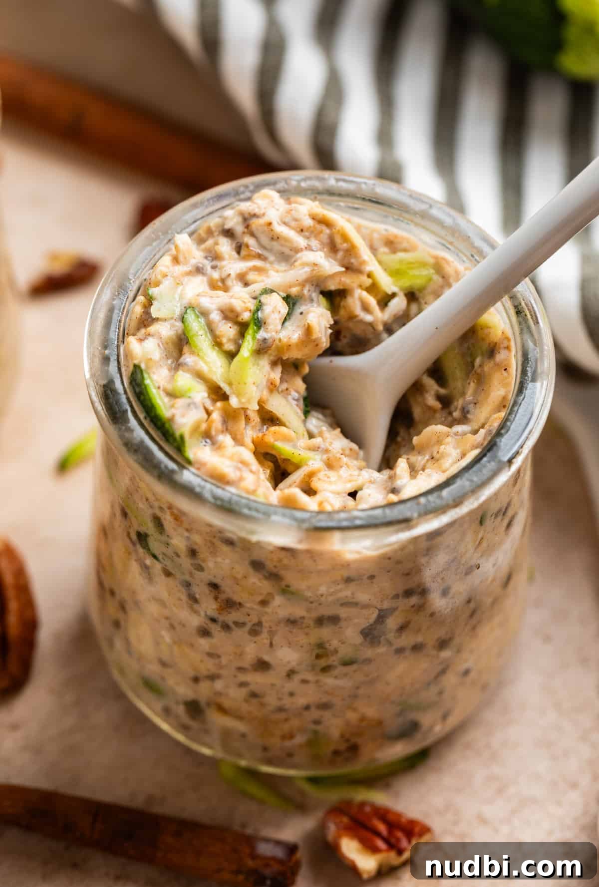 Overnight Zucchini Bread Oats — Moist, Spiced Breakfast Bowl 4 White spoon scooping into a jar of zucchini bread overnight oats.