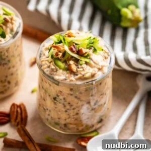 Overnight Zucchini Bread Oats — Moist, Spiced Breakfast Bowl 5 Glass jar with zucchini bread overnight oatmeal and white spoons beside it along with pecans and cinnamon sticks.