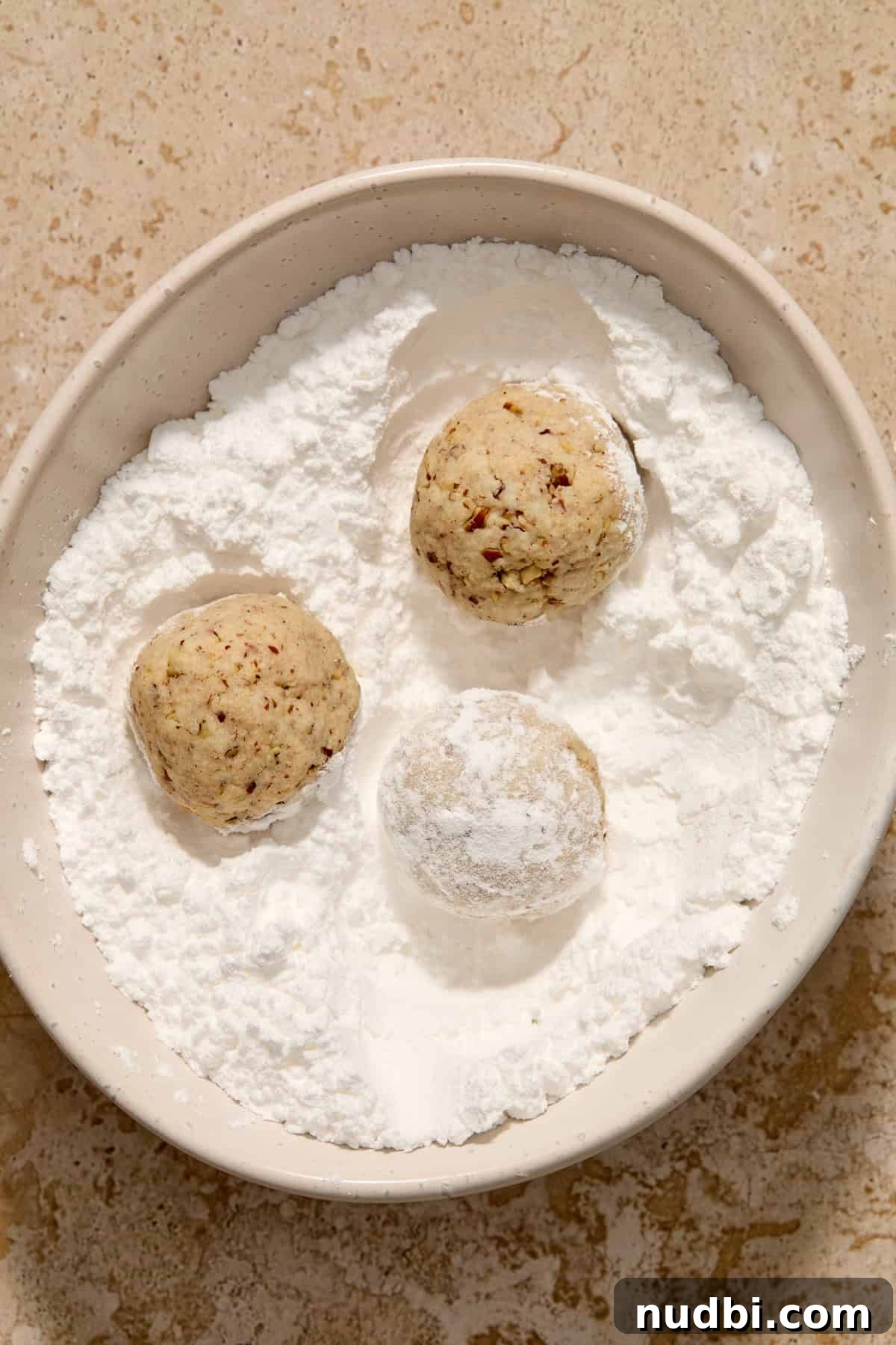 Cream Cheese Pecan Snowball Cookies for Christmas Baking 7 Snowball cookies rolled in powdered sugar in bowl.