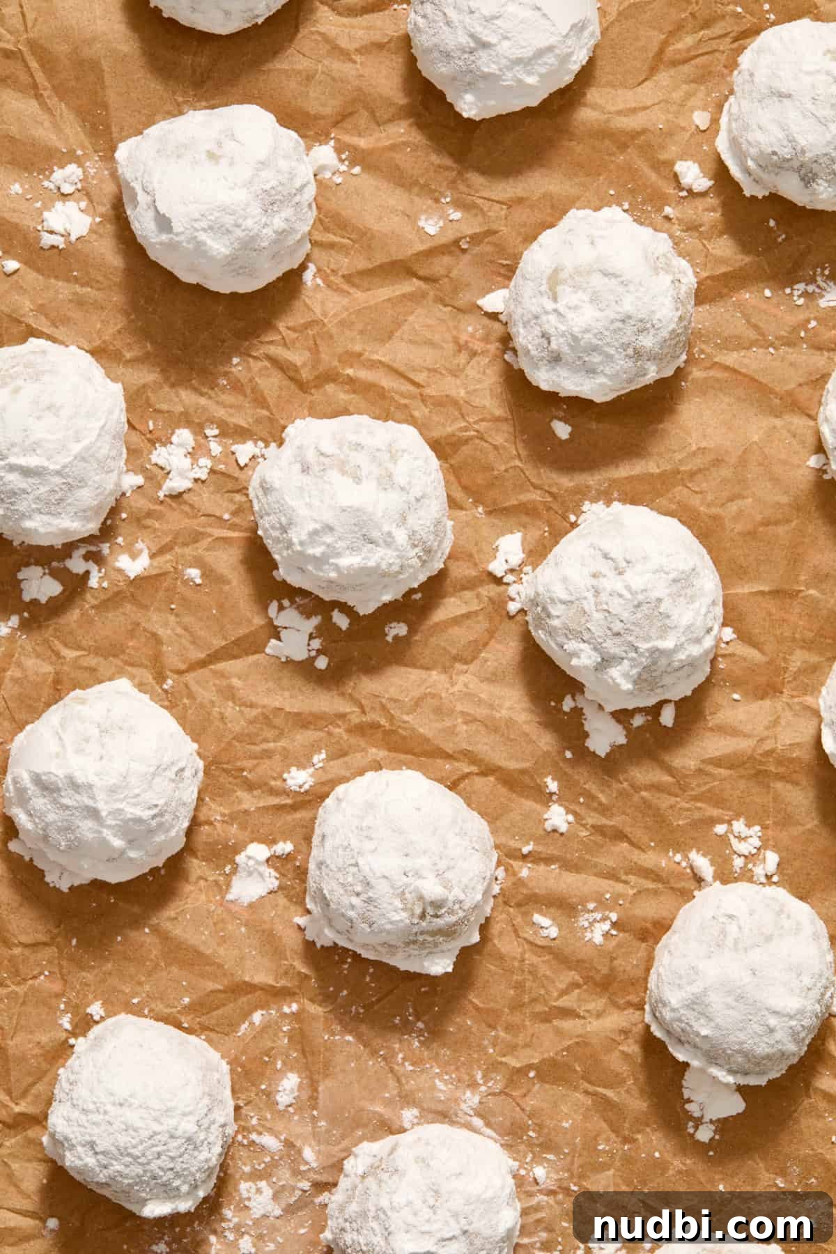 Cream Cheese Pecan Snowball Cookies for Christmas Baking 8 Parchment paper with powdered sugar covered cookies arranged.