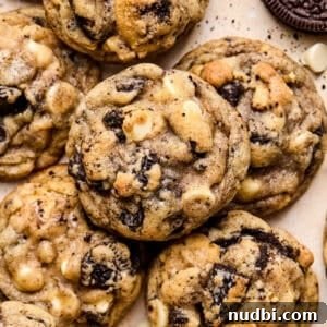Oreo Chocolate Chip Cookies Recipe — Crispy Edges, Chewy Center 17 Oreo chocolate chip cookies arranged on surface with white chocolate chips and crumbs around them.