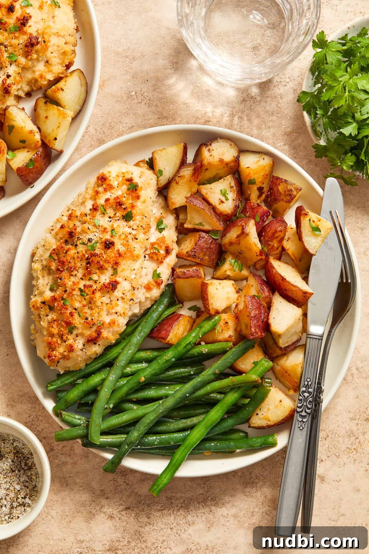 Parmesan-Crusted Chicken Sheet Pan Dinner Recipe 11 Parmesan baked chicken, roasted potatoes and green beans on white plate with fork and knife.
