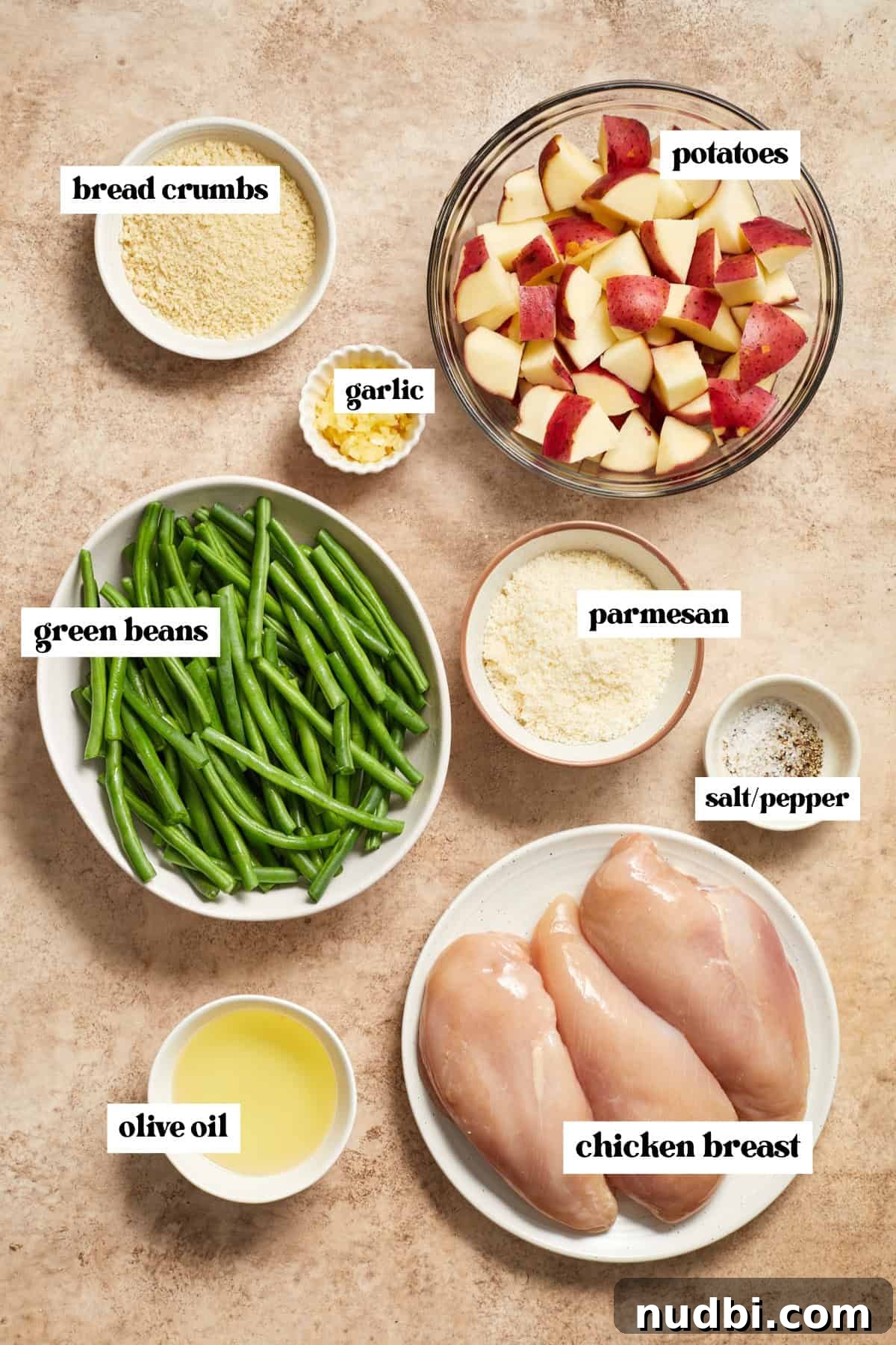 Parmesan-Crusted Chicken Sheet Pan Dinner Recipe 4 Chicken breast, green beans, potatoes, olive oil, parmesan and other labeled ingredients needed for recipe on surface.