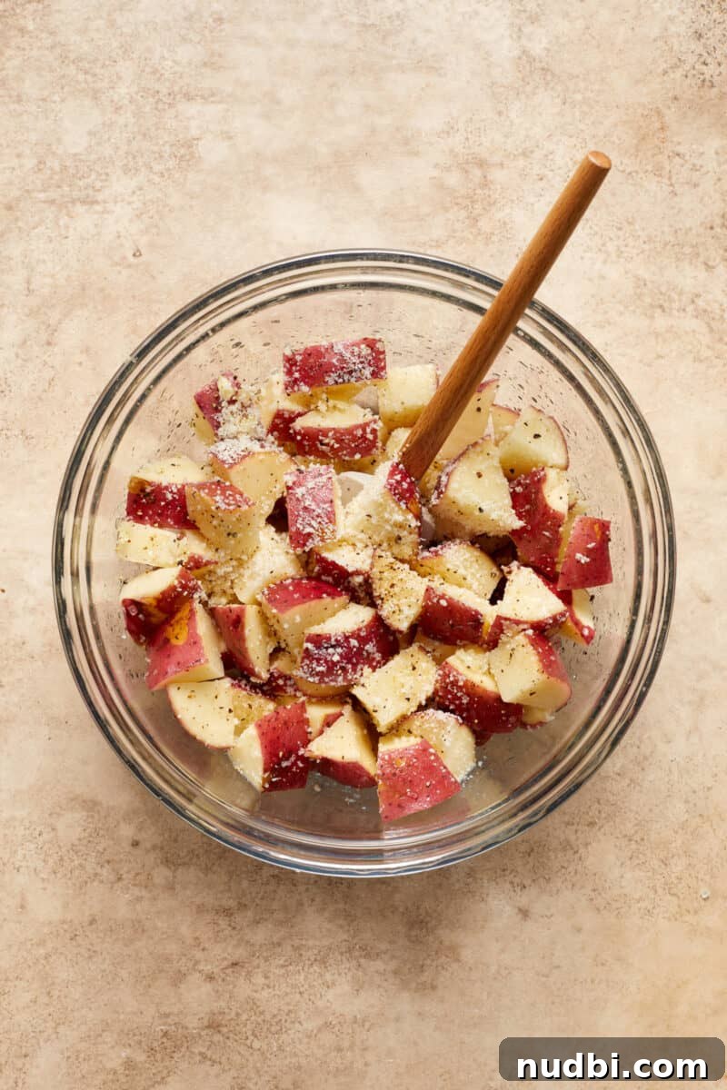 Parmesan-Crusted Chicken Sheet Pan Dinner Recipe 5 Quartered red potatoes in glass bowl with seasoning and parmesan and spatula.