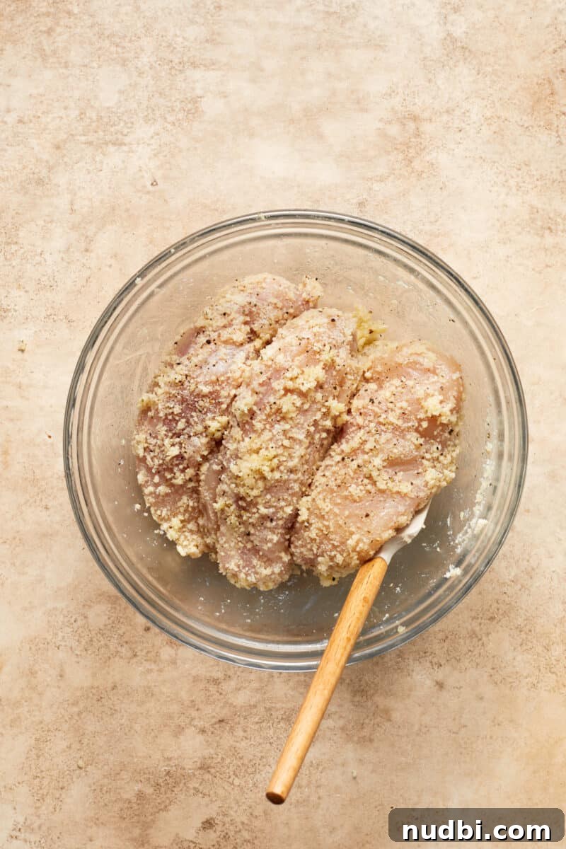 Parmesan-Crusted Chicken Sheet Pan Dinner Recipe 7 Chicken breast in glass mixing bowl tossed with parmesan, breadcrumbs and seasoning.