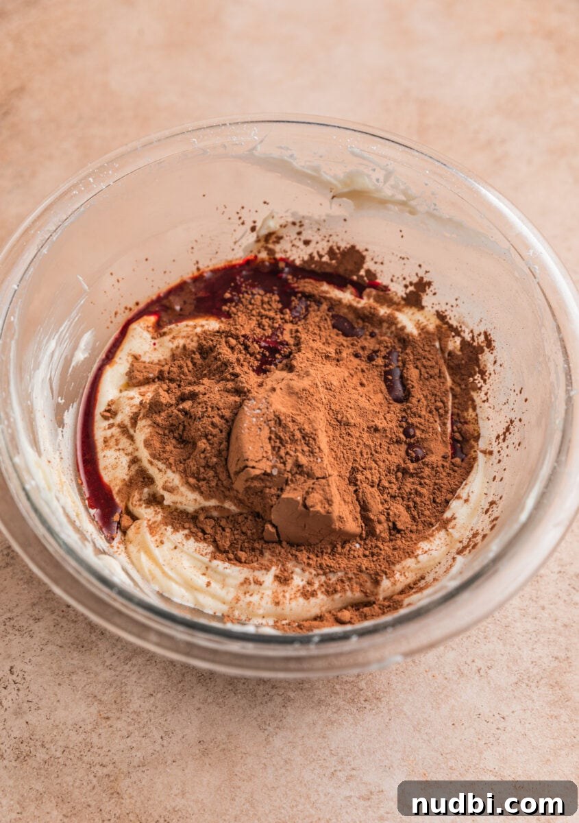 Red Velvet Cheesecake Dip Recipe — Creamy Party Dessert Dip 6 Cocoa powder, vanilla and red food coloring added to creamed cream cheese in glass bowl.