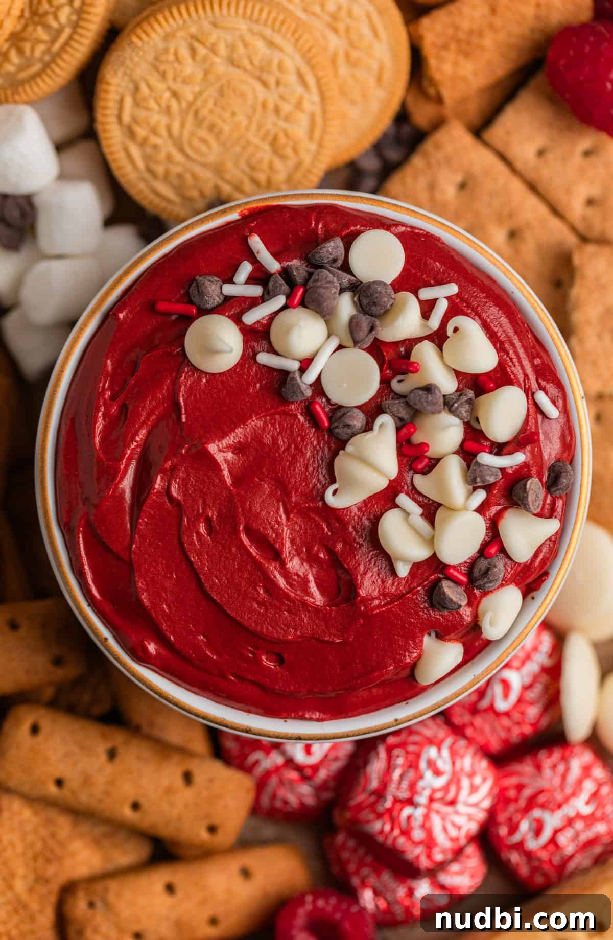Red Velvet Cheesecake Dip Recipe — Creamy Party Dessert Dip 10 Red velvet cheesecake dip in bowl topped with sprinkles and chocolate chips surrounded by cookies, graham crackers and other dippers.