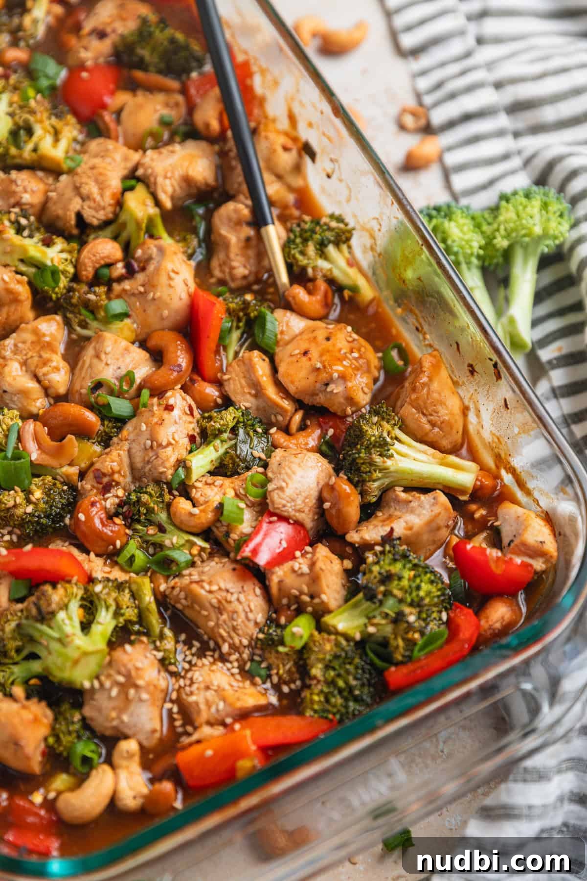 Crispy Baked Cashew Chicken with Garlic Soy Glaze 2 Glass baking pan with easy cashew chicken recipe and spoon scooping into it.