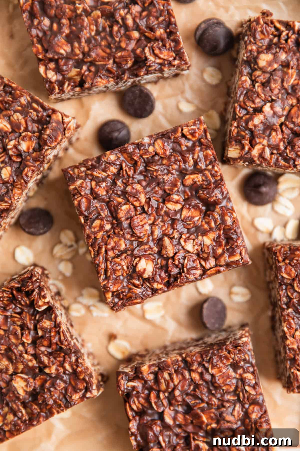 No-Bake Peanut Butter Chocolate Oatmeal Bars Recipe 2 No bake peanut butter chocolate oatmeal bars arranged on parchment with chocolate chips and oats surrounding.