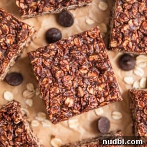 No-Bake Peanut Butter Chocolate Oatmeal Bars Recipe 10 No Bake peanut butter chocolate oatmeal bars on parchment with rolled oats and chocolate chips surrounding the bars.