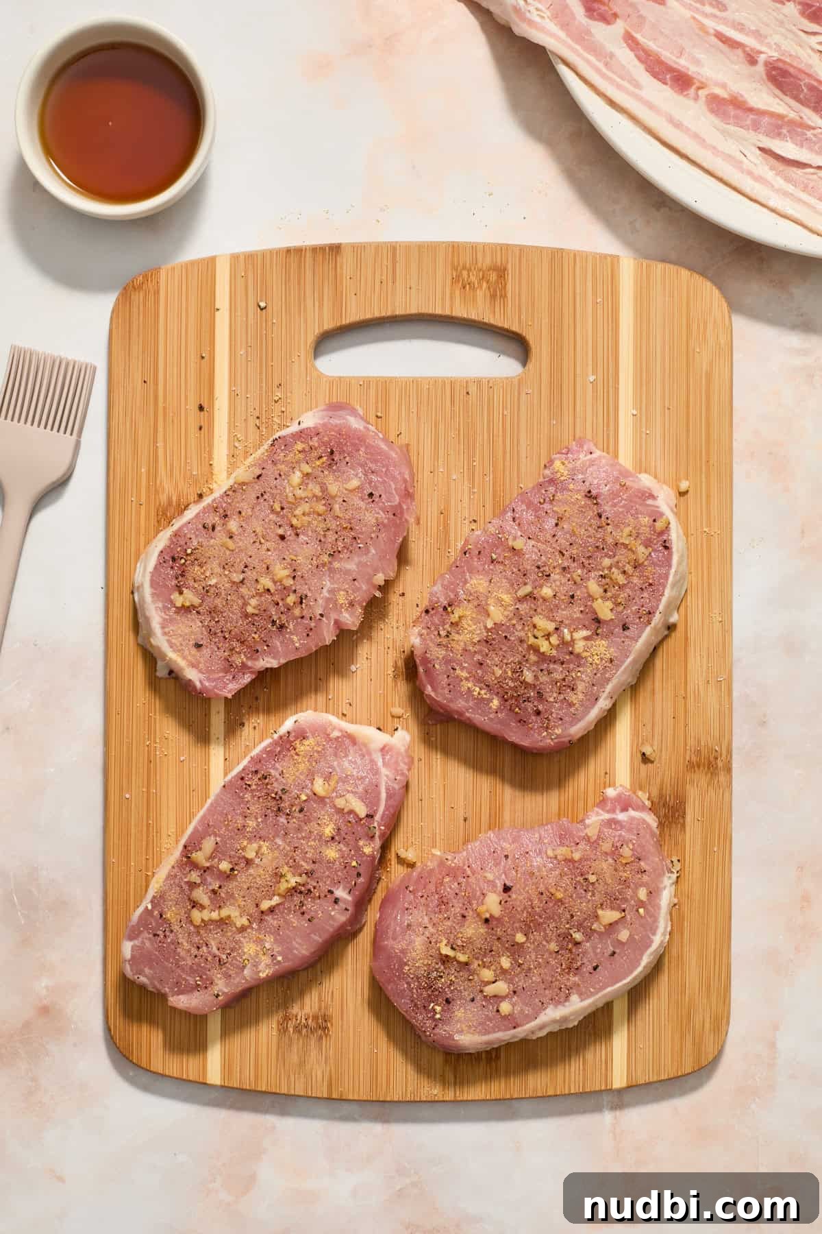Maple-Glazed Bacon-Wrapped Pork Chops with Crispy Edges 5 Seasoned pork chops on wood cutting board.