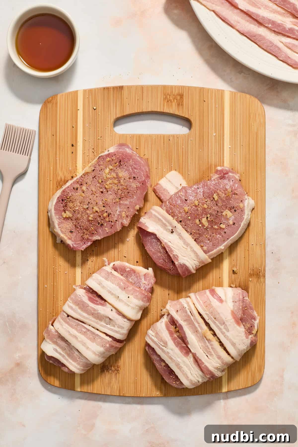 Maple-Glazed Bacon-Wrapped Pork Chops with Crispy Edges 6 Pork chops with bacon strips wrapped around on cutting board.