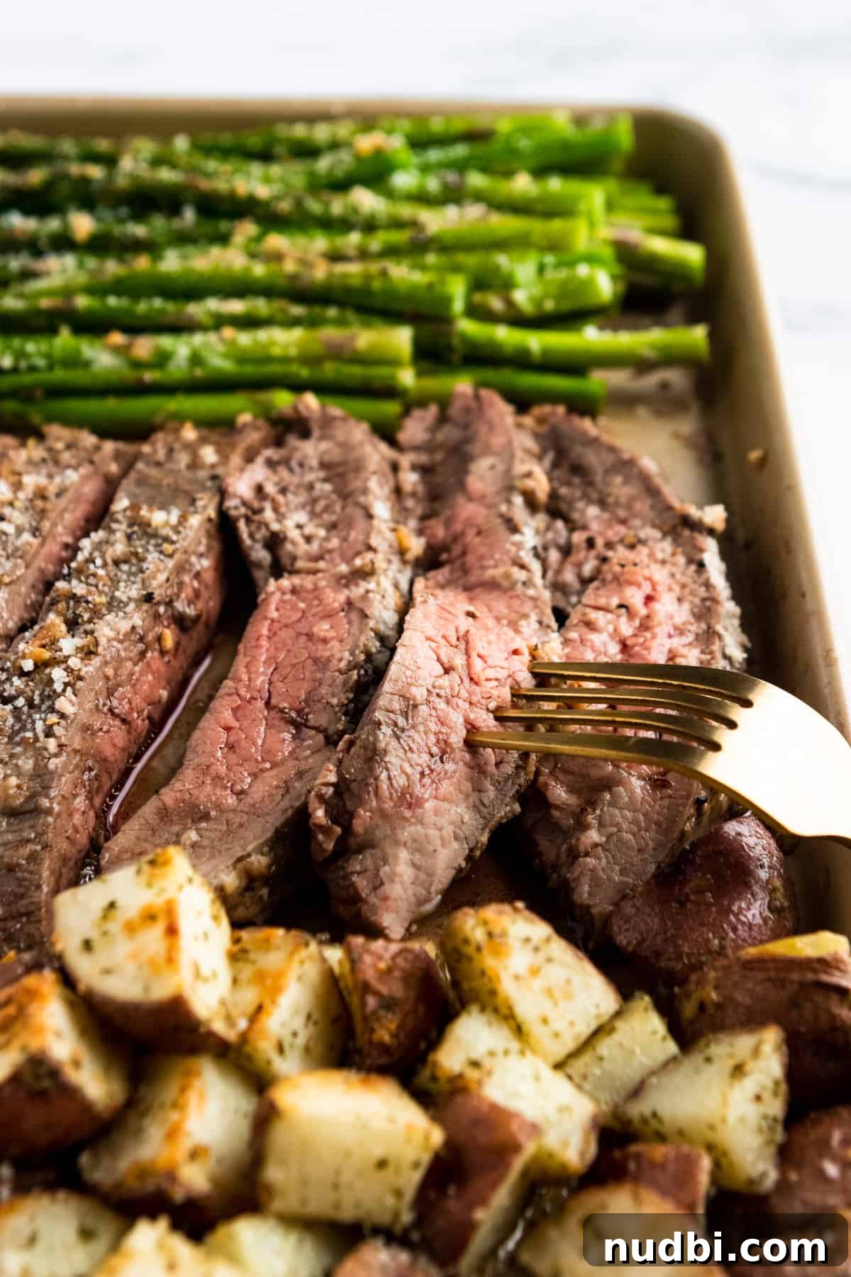 Parmesan-Crusted Steak and Roasted Potato Sheet Pan Dinner 2 Parmesan crusted Flank steak sliced on sheet pan with fork.