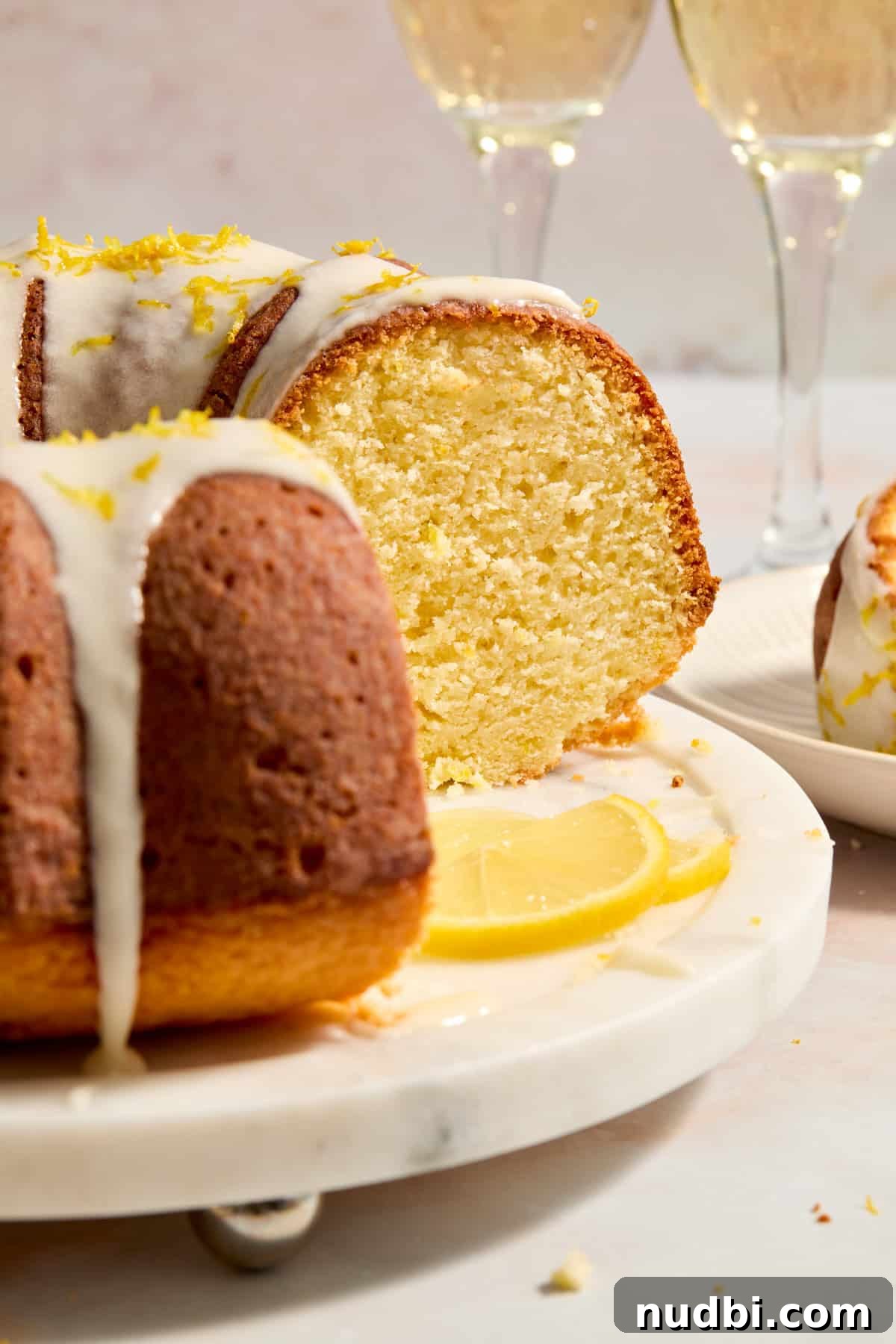 Champagne-Infused Lemon Bundt Cake Recipe 3 Lemon champagne bundt cake on cake tray with lemon glaze drizzled over top.