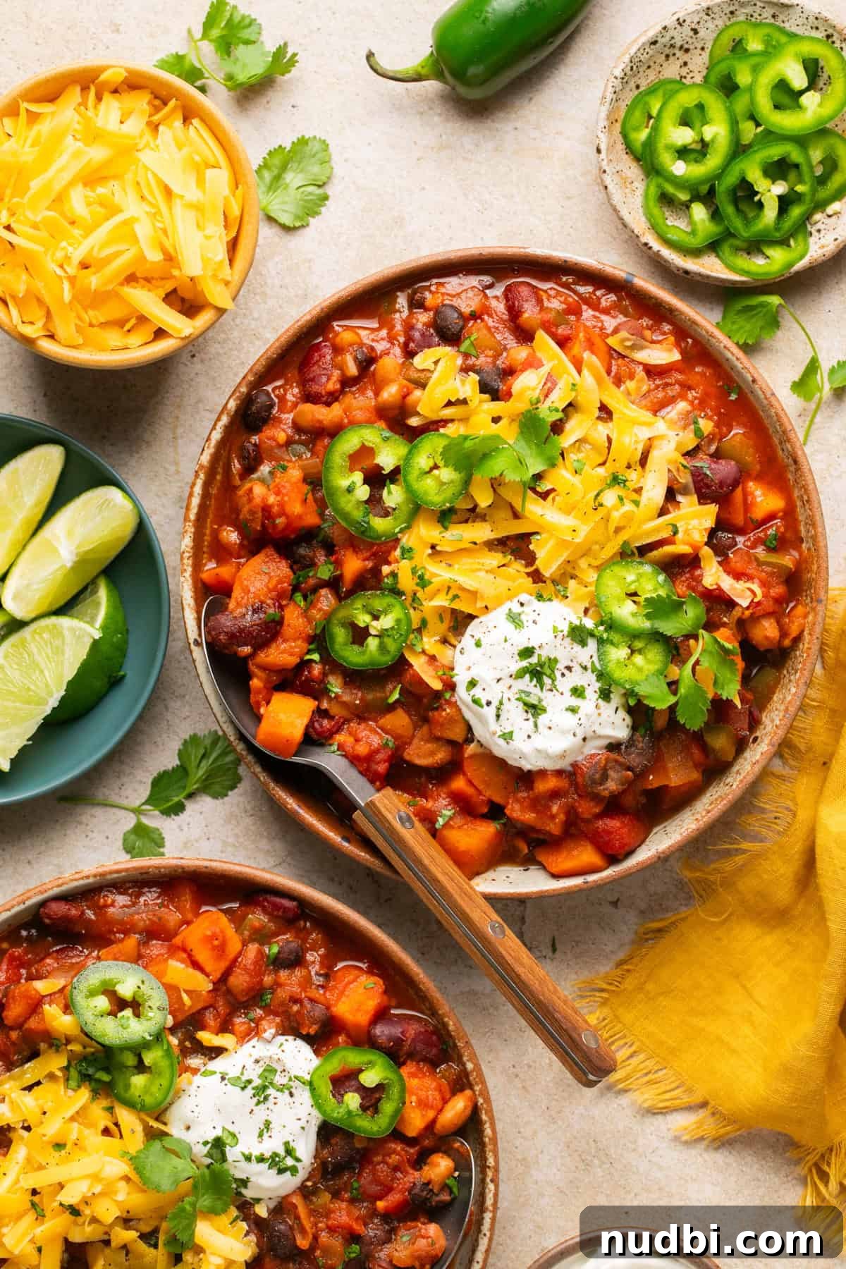 Slow Cooker Sweet Potato and Black Bean Chili Recipe 2 Bowl of sweet potato chili topped with cheese, sour cream, cilantro, etc. with spoon scooping into the bowl.