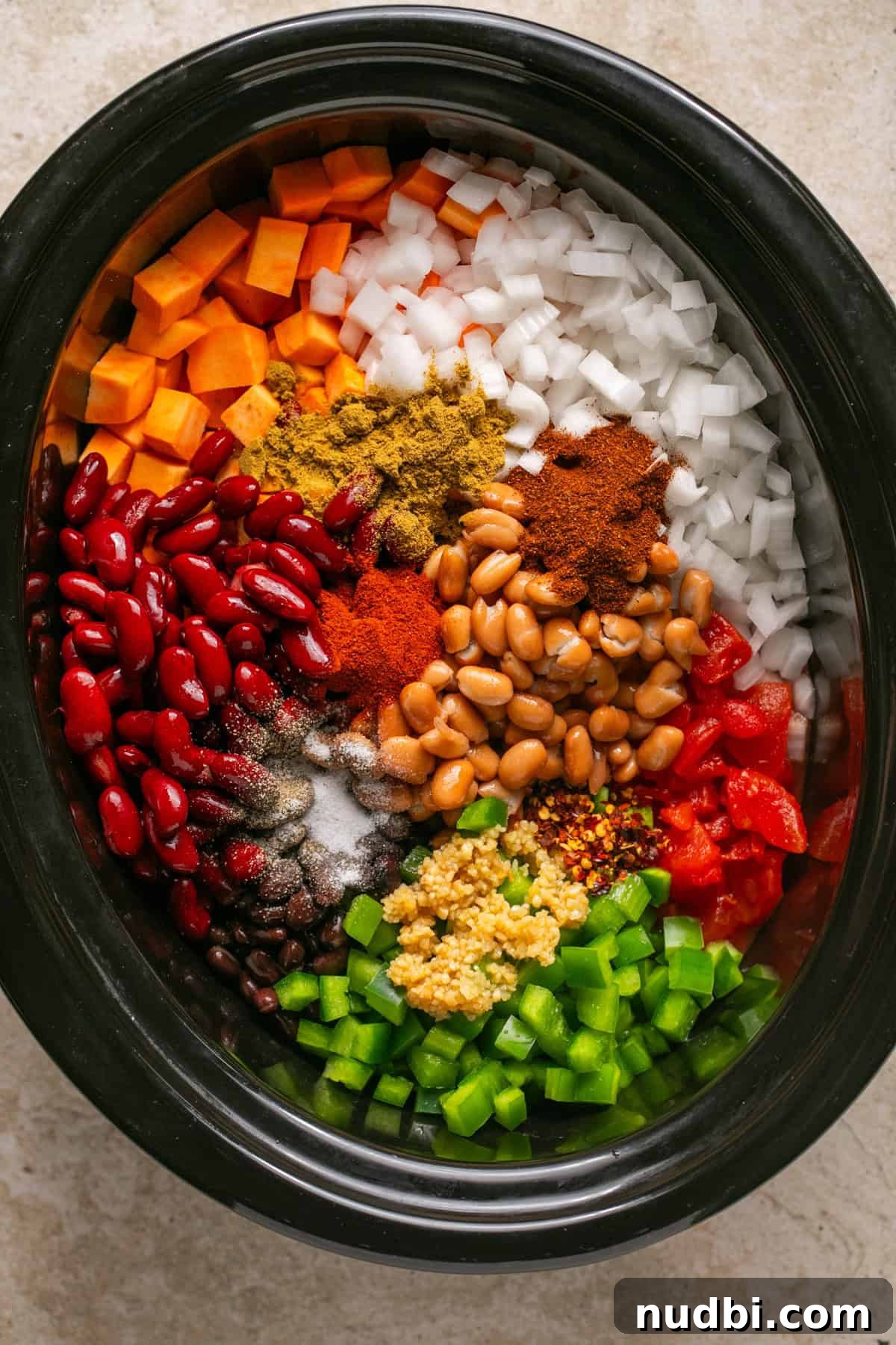 Slow Cooker Sweet Potato and Black Bean Chili Recipe 4 Cubed sweet potatoes, beans, green peppers, onion, spices and other ingredients arranged in slow cooker.