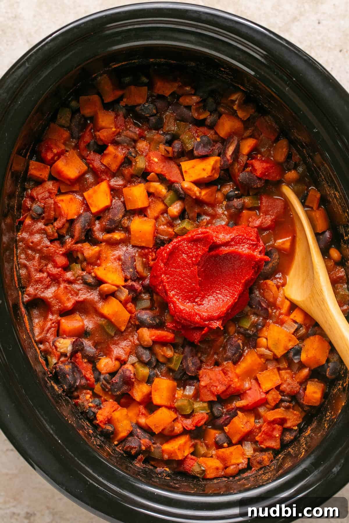Slow Cooker Sweet Potato and Black Bean Chili Recipe 6 Tomato paste added to chili in crock pot with wooden spoon.