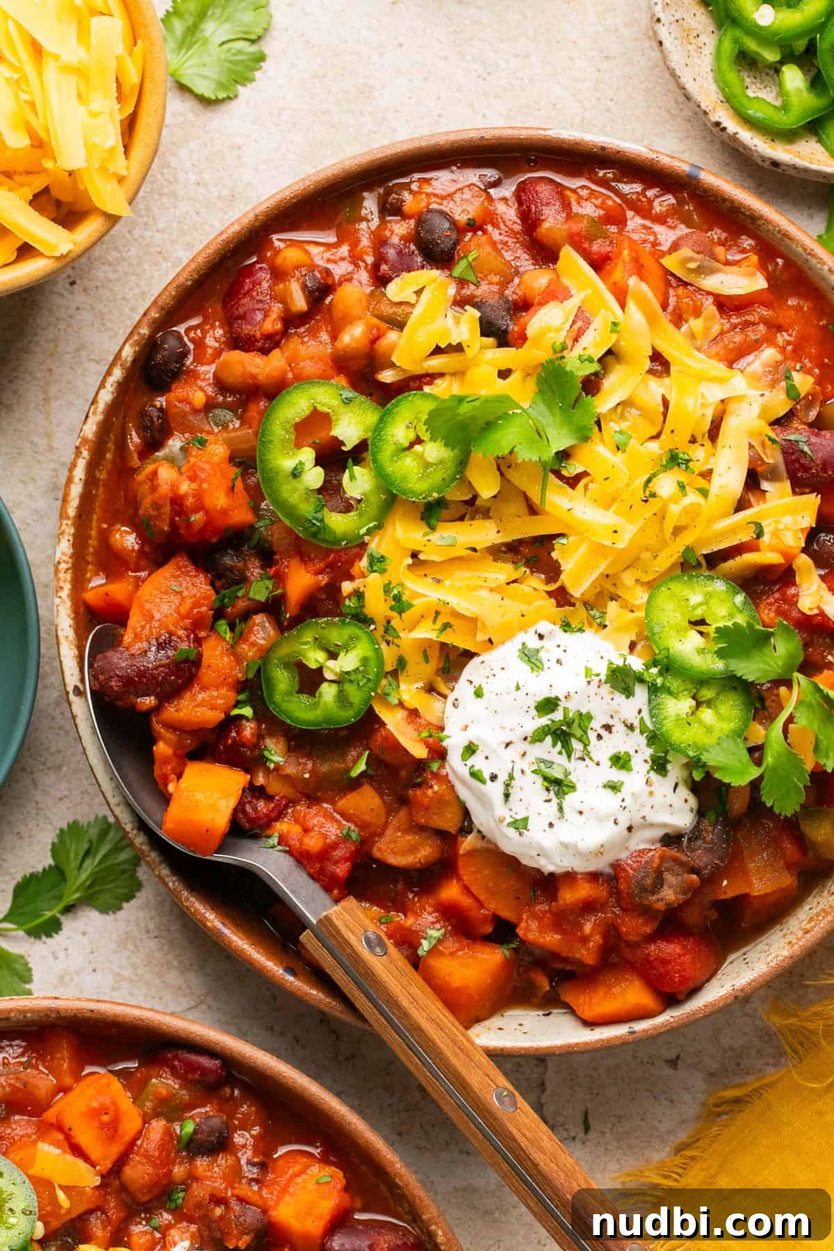 Slow Cooker Sweet Potato and Black Bean Chili Recipe 9 Overhead view of bowl with slow cooker vegetarian chili topped with cheese, sour cream, jalapeño and spoon scooping into the bowl.