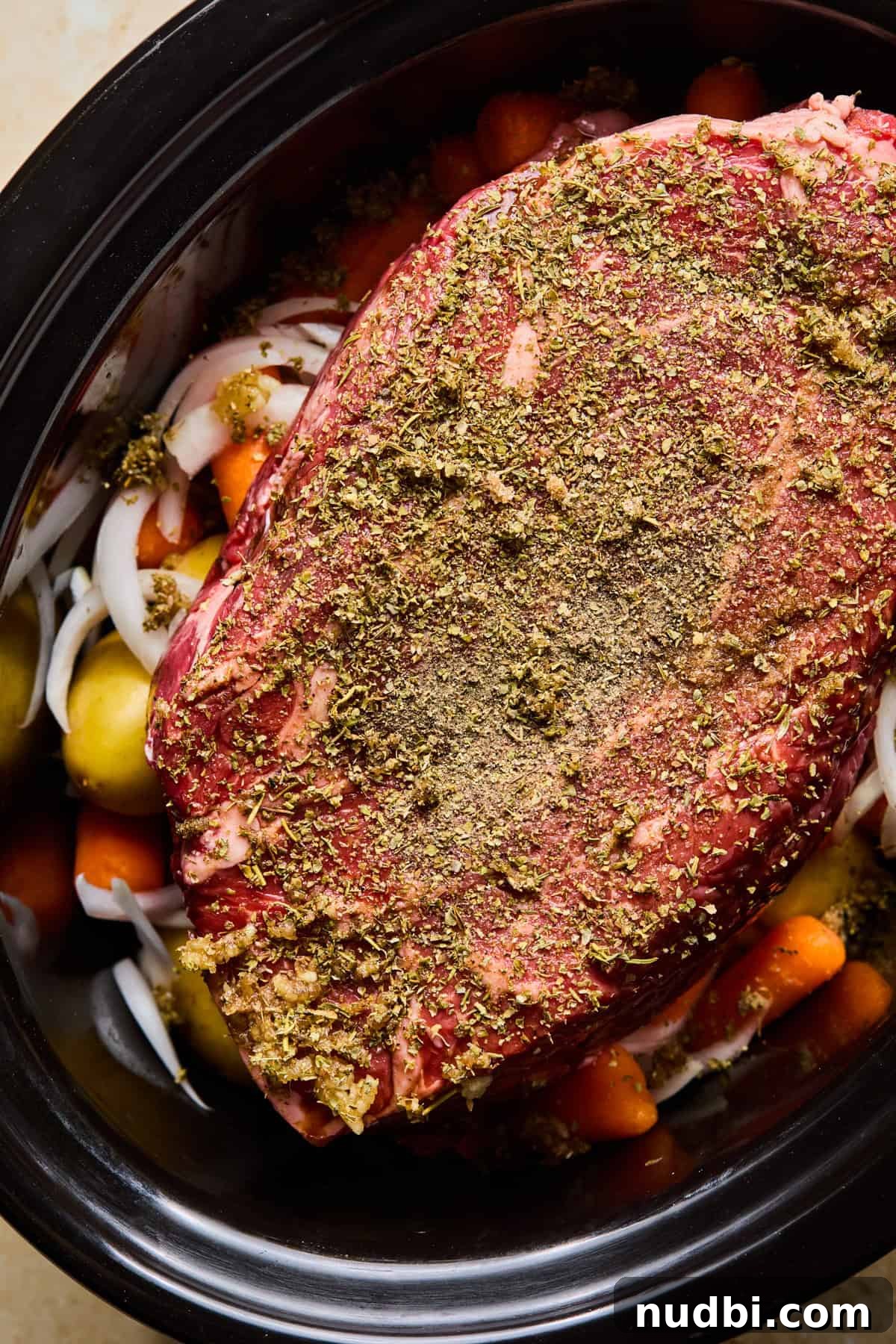 Slow-Cooked Chuck Roast Recipe for Tender, Juicy Beef 7 Chuck roast with herbs and seasoning on top of vegetables in crock pot before cooking.