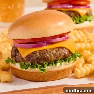 Crispy Air Fryer Hamburgers: Juicy Patties in Minutes 11 Air fried hamburger on bun with french fries on parchment lined wood surface.
