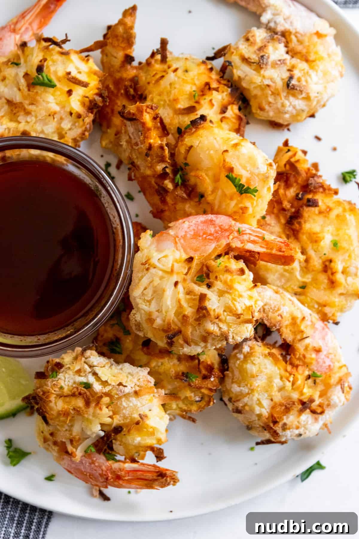 Air Fryer Coconut Shrimp with Honey Sriracha Dipping Sauce 2 Air fryer coconut shrimp on white plate with sauce and fresh parsley.
