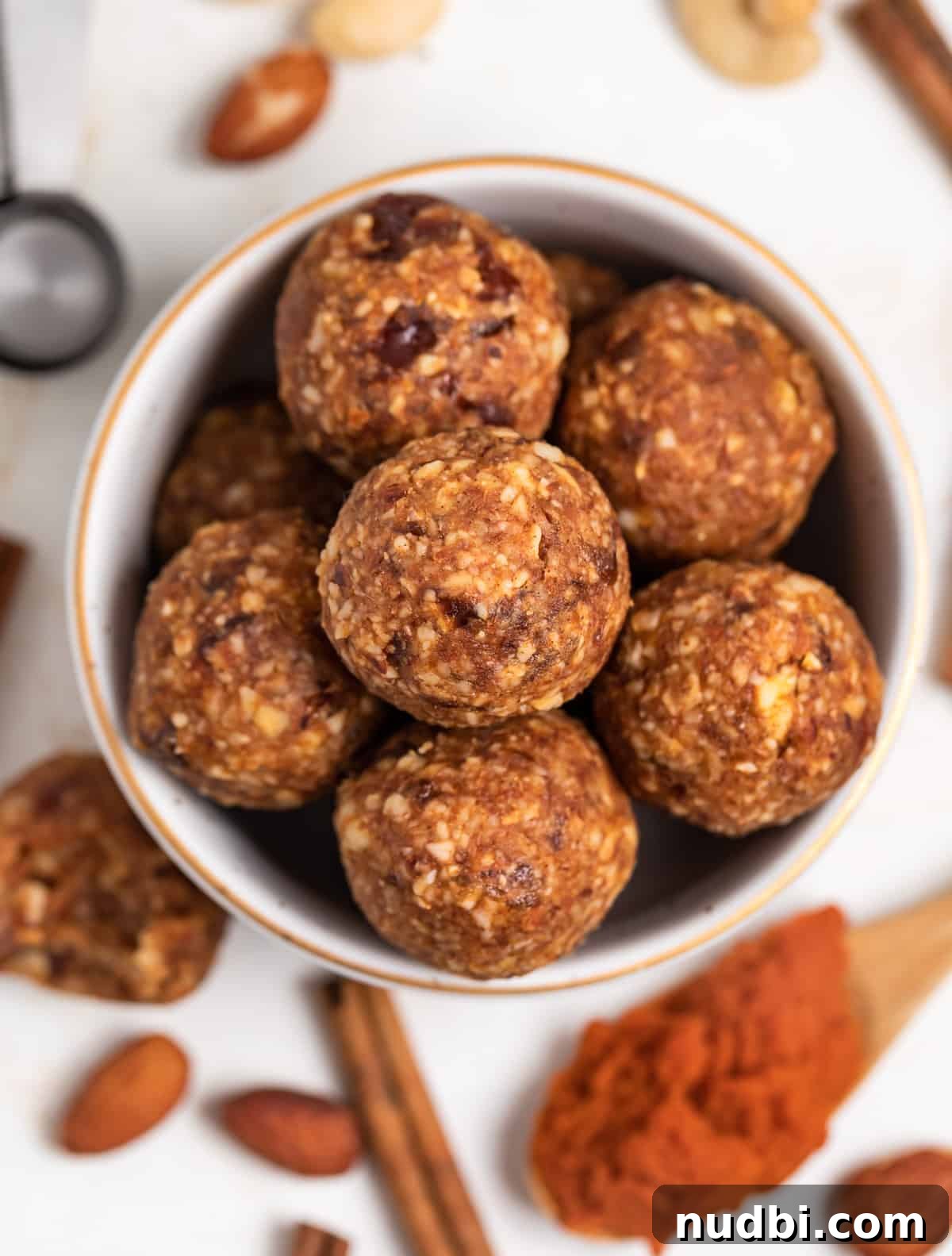 Pumpkin Pie Energy Bites: Fall Snack Recipe with Oats & Dates 2 Pumpkin energy balls in bowl with pecans, cinnamon stick, spoon of pumpkin and cashews surrounding.
