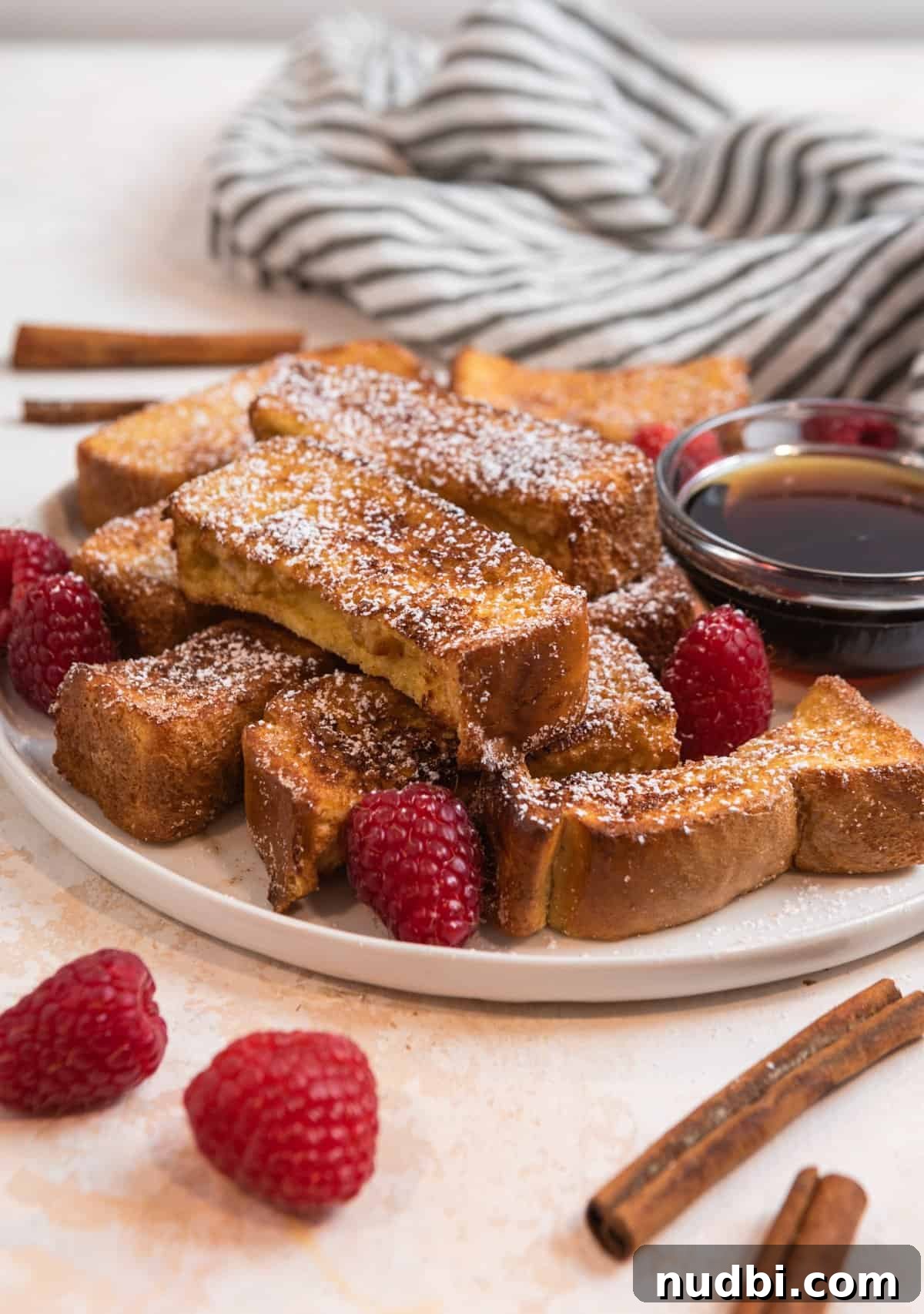 Crispy Air Fryer French Toast Sticks Recipe 2 White dish with air fryer French Toast sticks with powdered sugar and raspberries.