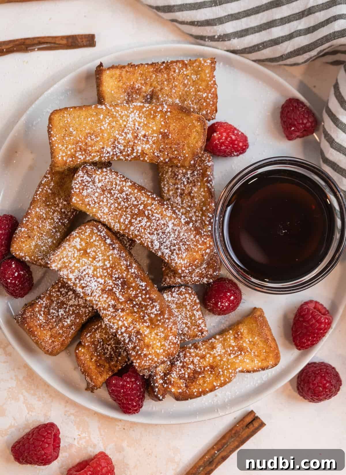 Crispy Air Fryer French Toast Sticks Recipe 3 Overhead view of plate of cinnamon sugar covered air fryer French toast sticks with maple syrup in glass bowl.